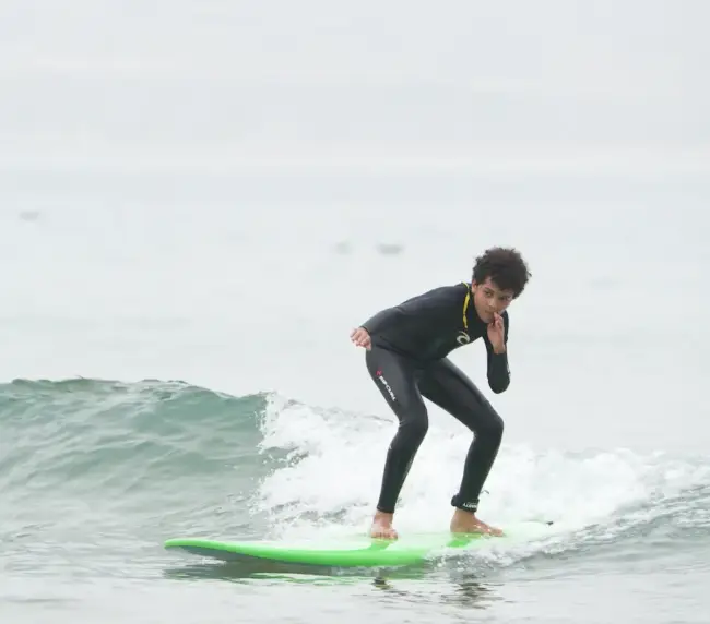Young surfer in a black wetsuit balancing on a green board while riding a gentle wave in Imsouane.