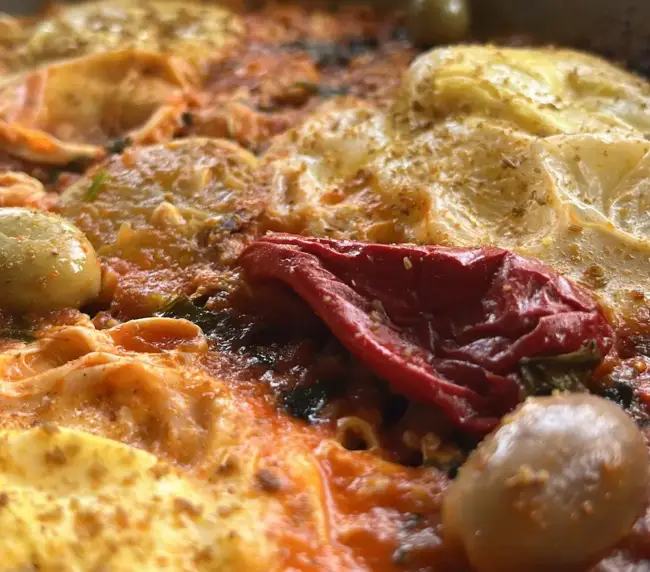 Close-up of a Moroccan Berber omelette with eggs, tomato, olives, and roasted pepper at an Imsouane surf camp.