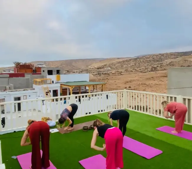 Five guests stretching on pink yoga mats across a rooftop terrace at an Imsouane surf house.