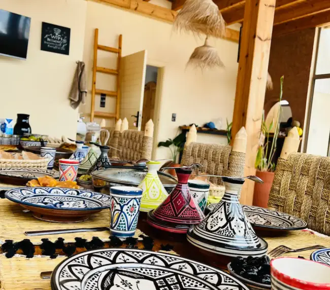 Colorful tagines and hand-painted dishes set for a shared meal at an Imsouane surf house.