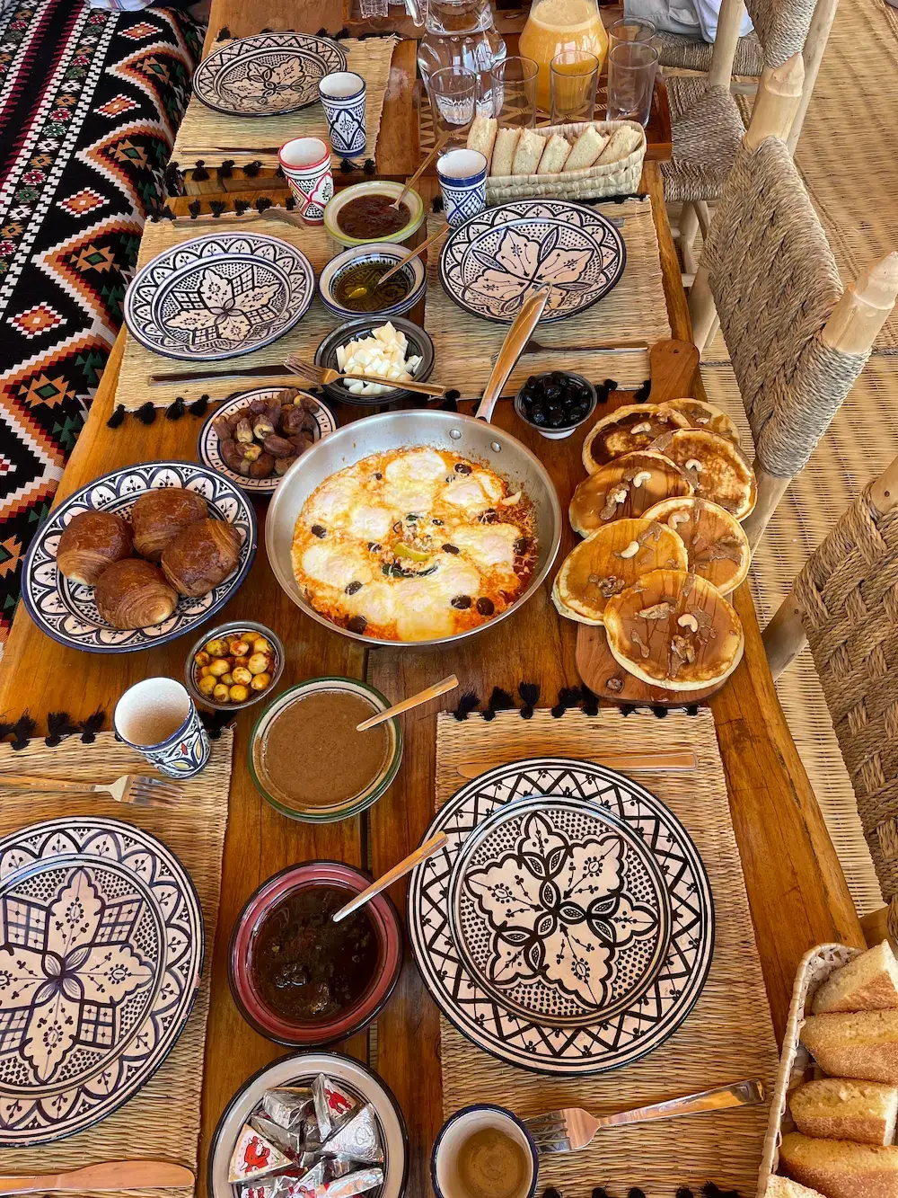 Breakfast table with eggs, pancakes, croissants, dates, bread, and juice at an Imsouane surf camp.
